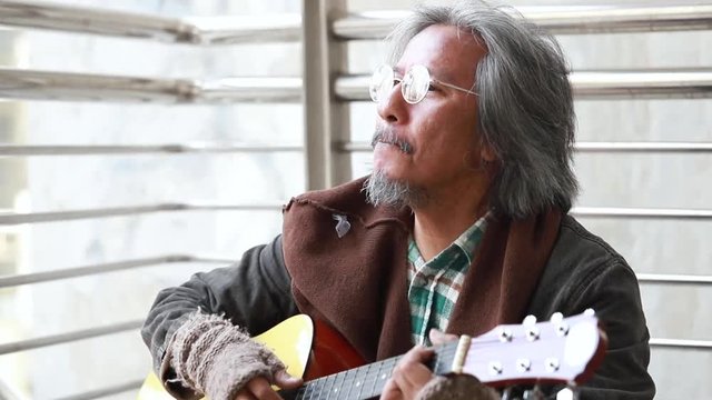 Senior homeless artist playing guitar to make money on street.
