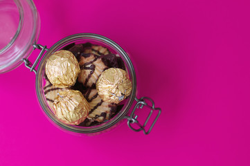 Sweets in foil and cookies in a glass jar on pink background. Jar with sweets, top view