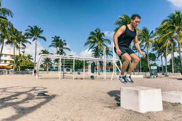 Squat jump on training box in outdoor beach gym. Man athlete training workout at Fitness bench jumping outside summer american South Beach Miami city. Strength training fit male working out outdoors.
