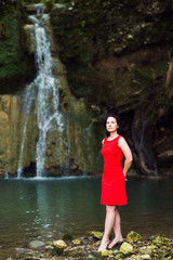 portrait of a brunette girl in a red dress at the waterfall