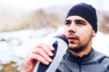 Young Athlete Drinking From Bottle While racing in Trail Run in Winter Day