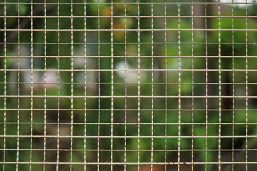 Obraz premium Fence Made Of Metal Mesh, Square Cells, Against A Background Of Blurry