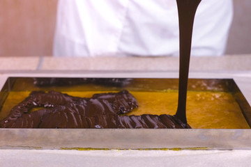 Preparation of filling for sweets. Liquid chocolate is poured on apricot marmalade.