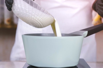 Cook pours the cream from the bowl into the saucepan to reheat. Hands in black gloves close-up.