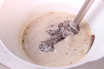 Mix liquid dark chocolate and cream in a white bowl with blender. Close-up view.