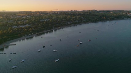 Motorboats on a lake, C4k aerial, drone shot, of  covered boats, anchored at the coast of lago di Garda, on a sunny, summer morning dawn, in Veron, Italy