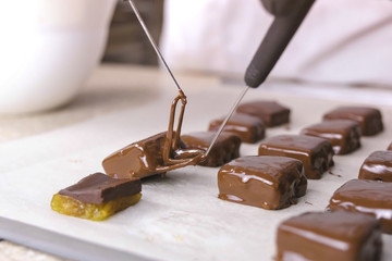 Baker dips candies in melted chocolate and put it on baker paper to dry. Production of chocolate...