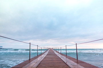 Obraz premium Wooden pier in the sea. Beautiful waves at sunset.