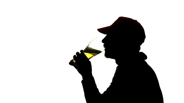 Bearded man in a cap drinks beer from a glass. Side view. Silhouette White background