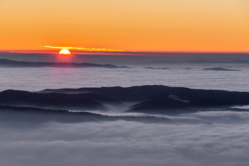 Obraz premium Beautiful sunset over a valley filled by fog with mountains and hills