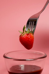 fondue strawberry soaked in hot black chocolate on a fork with pink background with minimalist...