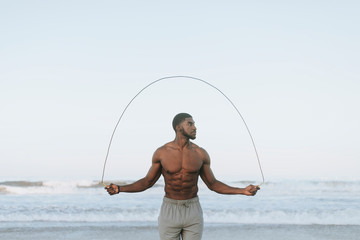 Fit man jumping rope at the beach - obrazy, fototapety, plakaty