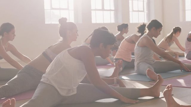 yoga class of beautiful multi ethnic women practice side seated wide angle pose enjoying healthy lifestyle exercising in fitness studio group meditation at sunrise