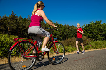 Healthy lifestyle - middle-aged woman riding bike and young man running