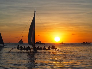 Beautiful silhouette of sunset in the sea and travellers on sailboat at Boraycay Philippinse.