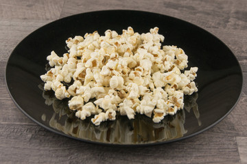 Home-cooked in the microwave the popcorn in a black bowl on a gray wooden table, front view