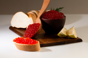 red caviar in a ceramic dish on a wooden platform on a white background