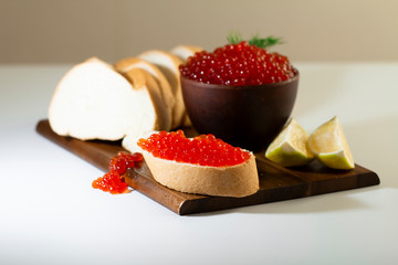 red caviar in a ceramic dish on a wooden platform on a white background