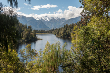 Fototapeta premium Lake Matheson on the West Coast of New Zealand surrounded by forest, with Mounts Cook and Tasman of the Southern Alps in the background.