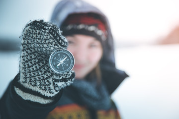 Young woman with gloves is holding up a compass, outside in the winter
