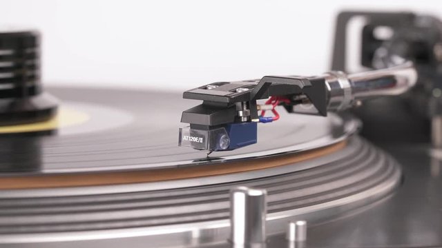 Close-up of LP turntable playing a vinyl. Cuing lamp, clamp, tone arm and coil cartridge atre on the foreground.