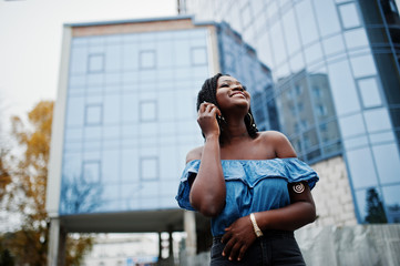 Attractive african american woman with dreads in jeans wear posed against modern multistory building.
