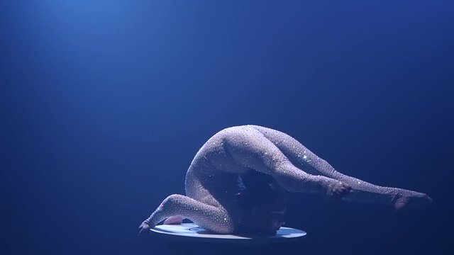 Girl acrobat on the table shows the tricks of standing on his hands. Smoke background. Slow motion