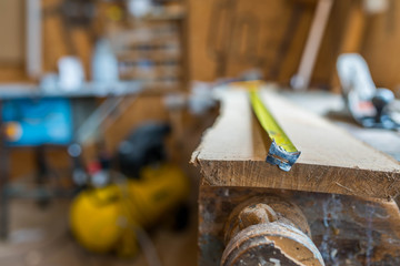 Tape measurer on long oak board in a small wood workshop, shallow depth of field.