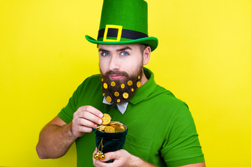 Happy young adult man male in green shirt, green leprechaun hat and tie bow with gold coins in...