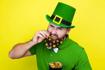 Happy young adult man male in green shirt, green leprechaun hat and tie bow with gold coins in...
