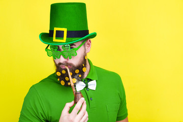 Happy young adult man male in green shirt, green leprechaun hat and tie bow with gold coins in...