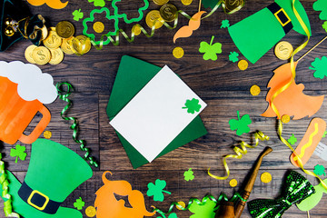 Blank postcard with green leprechaun lucky clover trefoil on green envelope on wooden background with props: green hat, gold coins, gifts, mustard sausage and glass of beer. Saint Patrick Day concept
