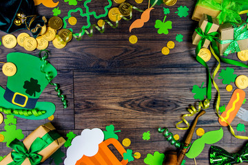 Saint Patrick Day concept. Paper Patrick day leprechaun props: green leprechaun hat gold coins, orange mustache and lucky clover trefoil as symbol of Ireland traditional holiday on wooden background