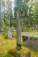 Cross at old semetery in Finland with grave crosses and stones.