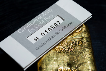 The certificate of assay for gold bars lies on a cast gold ingot. gehaltszertifikat für Goldbarren...