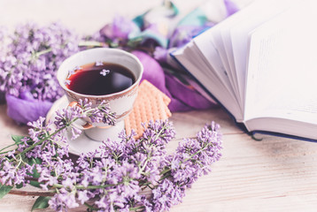Obraz na płótnie Canvas Morning cup of tee, cookies, book and lilac flower on wooden table from above. Beautiful breakfast. Flat lay style with copy space