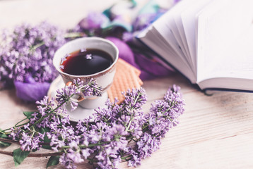 Morning cup of tee, cookies, book and lilac flower on wooden table from above. Beautiful breakfast. Flat lay style with copy space