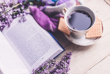 Morning cup of tee, cookies, book and lilac flower on wooden table from above. Beautiful breakfast. Flat lay style with copy space