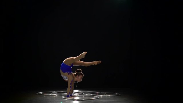 Gymnast stands on the hands performs acrobatic movements. Black background. Slow motion