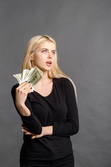 pretty blonde girl holds money in her hands, woman holds out money to you over grey background