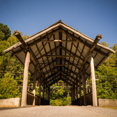 Covered wooden bridge in front of a forest in late summer, early autum, blue sky