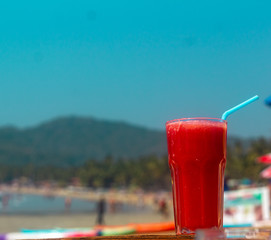 Beach smoothie Red watermelon juice on the beach with shacks and umbrella background