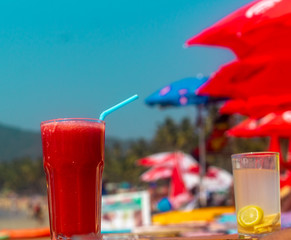Beach smoothie Red watermelon juice on the beach with shacks and umbrella background