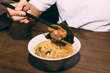 Hand pinching Chashu Pork in Hakata style Shio Chashumen (Salt soup) with chopsticks including noodle, sprout, seaweed and scallion. 