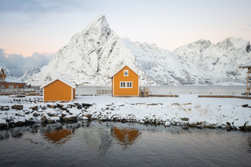 Yellow fishing rorbuer builded from wood on the white snow of winter with mountain view on the background in Reine village at Lofoten Norway