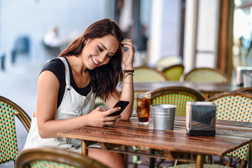 Smiling woman with blue eyes sitting on urban cafe using smart phone