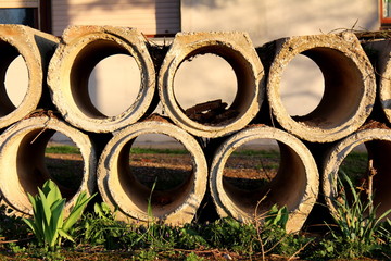 Concrete sewer pipes put on one pile in front of house and left until needed with grass and flowers in front at sunset