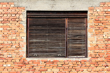 Cracked wooden window blinds on old dilapidated window frame mounted on red brick and concrete wall...