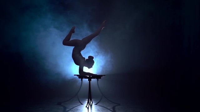 Acrobat girl executes tricks . Smoke background. Slow motion. Silhouette