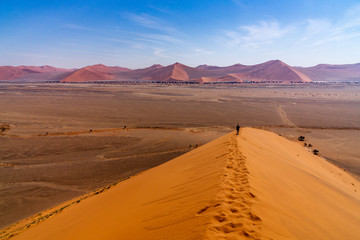 Fototapeta na wymiar Tourist walking on the scenic dunes of Sossusvlei, Namib desert, Namib Naukluft National Park, Namibia